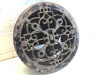 Front view shows the round vent with ornate Victorian-style floral and scrollwork grille design, some paint wear and patina.