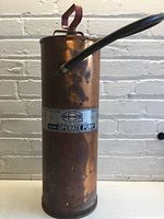 Front view of the copper extinguisher showing the cylindrical body, hose, and label with brand and operating instructions.