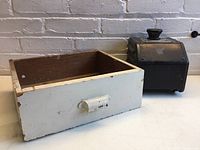 Photo showing white wooden vintage drawer and black metal printing industrial accessory with concrete base.