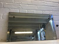 Full front view of rectangular mirror on a brick wall, showing overall shape and beveling.