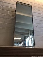 Front view of the vintage mirrored medicine cabinet showing full mirrored door with chrome edge trim, mounted against a brick wall.