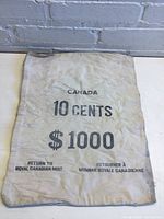 Front side of vintage Canadian cloth money bag showing printed text indicating it holds $1000 in 10 cent coins and return instructions to Royal Canadian Mint.