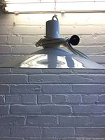 Side view of white metal hanging light fixture showing the conical shade and cord coiled around the top with switch.