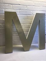 Front view of the gold painted wood letter "M" showing smooth surface and geometric design
