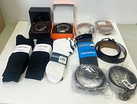 Photo showing two black Calvin Klein socks, one white low-cut sock, multiple belts in boxes, and belts rolled up with tags or packaging.