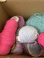 Top view of various yarn balls in a cardboard box shows multiple colors and textures, including smooth and sparkle yarn varieties.