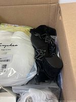 Box containing a white memory foam pillow and black heeled sandals with rhinestone bows