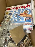 Box showing Spirograph kit and multiple miscellaneous items in original or mixed packaging.