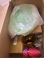 Photo of green decorative glass plate wrapped in bubble wrap, amber glass bowl, and purple glass bowl inside a large box