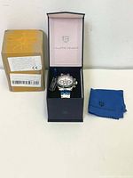 Watch in open black box with soft interior and Pagani Design branding, blue cleaning cloth beside it and original shipping box on left