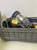 Grey plastic stacking tote containing Dyson ball vacuum main heads, hoses and parts with a yellow 'used' sticker on one main head.