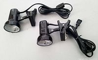 Two small black clip lamps with cords and clamps shown from side angle on white background.