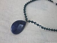 Close-up of the faceted large lapis teardrop pendant with small blue crystal beads on the chain.