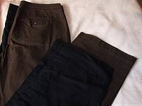 Two pairs of brown and black linen pants laid flat showing back and front details