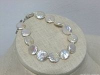 Coin pearl bracelet displayed on light beige fabric stand showing round, flat pearls with one irregular pearl clearly visible.