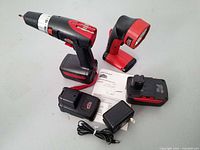 Side angle view showing the cordless screwdriver, work light, two batteries, charger, and instruction manual on a white surface.