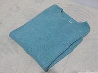 Folded blue knit sweater laid on light fabric, showing full item