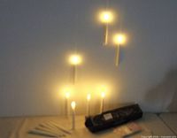 LED floating candles lit and suspended from nylon threads to simulate floating flames, with some candles standing on a surface and a remote control wand nearby.