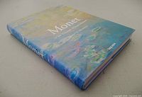 Front and spine view of Monet art book with cover featuring Monet's water lilies painting in soft pastel colors.