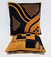 Front view of the two suede leather pillows stacked showing geometric checkerboard patterns and tassels on bottom pillow.