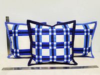 Set of three square patchwork pillows made from blue, navy, light blue and white silk moire fabric, arranged upright with rulers visible to show approximate size.