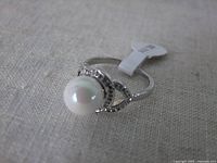 Close-up photo of the ring placed on fabric showing pearl center, zirconias, and size 10 tag.