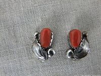 Top-down view of the pair of Simplicio Mexico 925 sterling silver clip-on earrings. Oval coral stones with surrounding silver leaf detailing clearly visible.