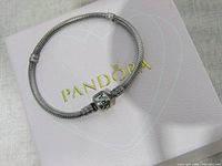 Full view of the silver Pandora charm bracelet on a white Pandora box with gold logo.