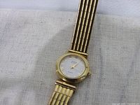 Gold tone Anne Klein wristwatch showing dial with Roman numeral hour markers and gold tone hands on white face.