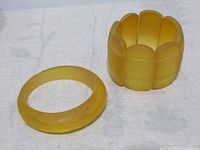Top view of the two yellow Bakelite bracelets on a white fabric surface, showing the solid bangle and the segmented stretch bracelet.