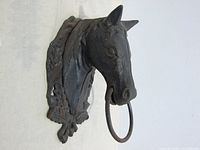 Front view of the vintage cast metal horse head with an attached metal ring for tie-ups, showing detailed mane and facial features.