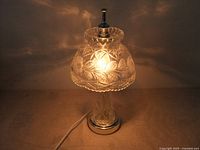 Small vintage crystal table lamp lit, showing etched floral and starburst decorations on the shade and wall reflections.
