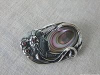 Front view of the vintage sterling silver brooch showing the profile of a woman with flower and garnet details, and the mother of pearl inlay.