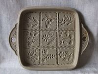 Front view of square stoneware shortbread pan with nine embossed designs and heart-shaped handles