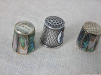 Three vintage thimbles displayed upright showing tops and inlay detail