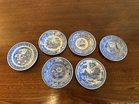 Photo showing top view of 6 small teacup saucers with various blue transferware designs on white porcelain.
