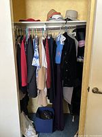 Photo of a closet rod with hanging vintage clothing and shelf with assorted hats above it.