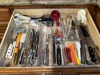Top view of kitchen drawer showing various kitchen utensils and cutlery organized in plastic compartments.