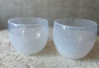 Two white gradient hand blown glass cups side-by-side on lace cloth.