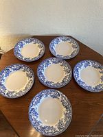 Top down view showing all 6 Spode Delamere plates arranged in a ring on a wooden table, highlighting size and pattern consistency