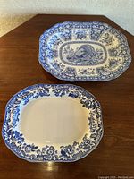 Photo showing two large rectangular platters on wooden surface, one with central turkey motif and floral blue border, the other with floral blue border only.