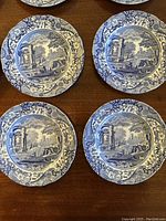 Four of the Spode Italian blue and white plates with scenic design arranged on a wooden surface, showing detailed border and central imagery.