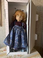 Red-haired Götz Fanouche doll in original box wearing floral pinafore and purple top.