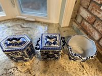Top view of two square blue and white porcelain jars with lids and side handles, along with the top edge of the porcelain vase.