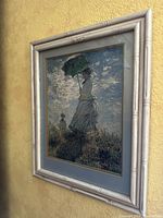 Full view of framed vintage painting showing a woman with parasol on grassy hill against a cloudy sky.