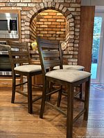 Three vintage ladder back barstools arranged on a kitchen floor with visible brick and wood cabinetry background.