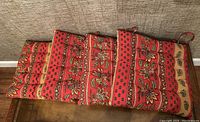 Set of four red floral patio chair cushions placed on the floor showing full length and pattern.