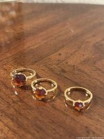 Three gold rings with amber-colored round stones of decreasing size lined up on wood surface.
