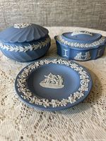 Three blue Jasperware Wedgwood pieces on lace fabric showing details and relief decorations.