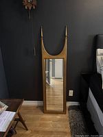 Full view of the mirror leaning against a wall showing its overall shape and design with tall finials and crescent-shaped top.